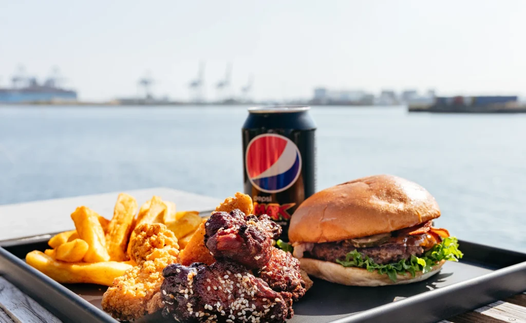 Burger, kyllingevinger og pommes frites med havnen i baggrunden